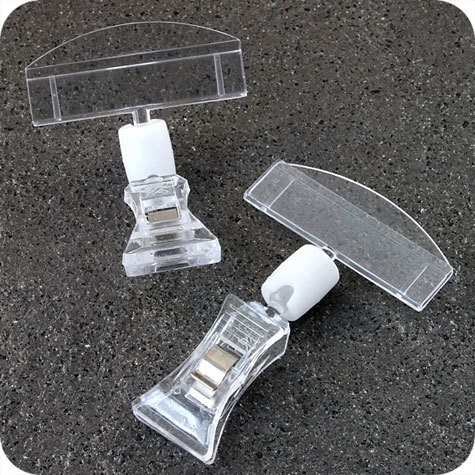 legatoria Doppia molletta Piccola-Portacartellino altezza 85mm TRASPARENTE in policarbonato. Composta da 2 mollette, 1 PICCOLA (38x21mm) e 1 PORTACARTELLINO (50x15mm) collegate da giunto a sfera. Altezza totale 78mm.